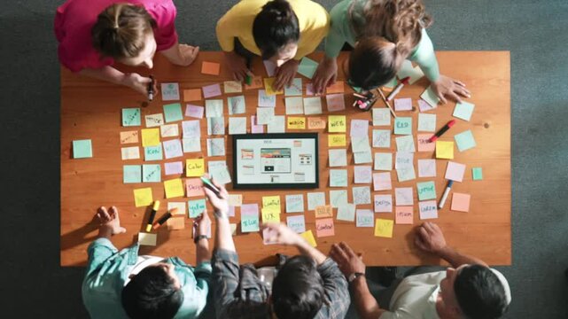 Aerial view of developer team discussing and showing digital program and writing by using Ux Ui design. Top down view of business people develop wireframe prototype for phone and computer. Symposium.
