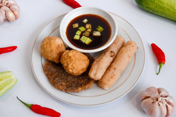 A plate of pempek (indonesian fish cake) with a variety of items including adaan (ball shaped), lenjer (long shape), and kulit (circle). The plate is set on a white background.