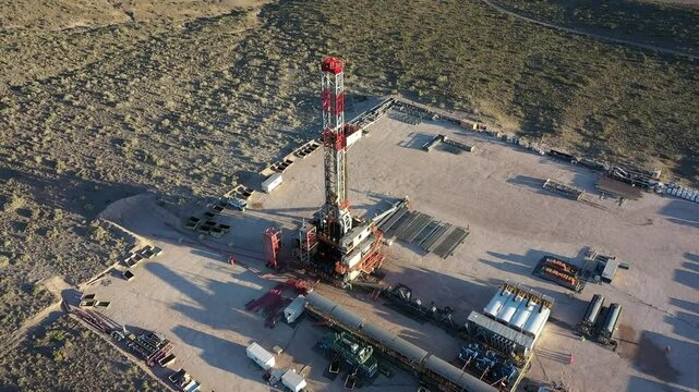 Drone flies over a drill for oil and gas drilling and is projected over the Patagonian steppe of Vaca Muerta. Trailers and trucks can be seen