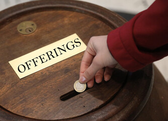 hand of girl putting european coin into the offering box