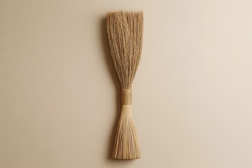 A simple broom made of natural straw against a neutral background