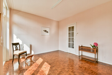 A bright, minimalist interior featuring a wooden floor, a single chair, and subtle decor elements that emphasize spaciousness and natural light.