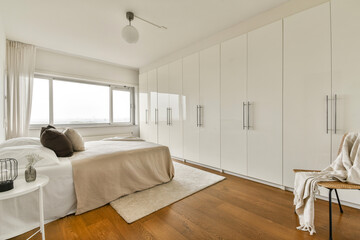 A sleek and stylish bedroom featuring white cabinetry, warm wooden flooring, and cozy textiles, creating a serene and inviting atmosphere.
