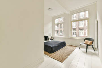 A bright and airy modern room featuring minimalist design elements. The room's decor includes large windows and a stylish rug on white flooring.