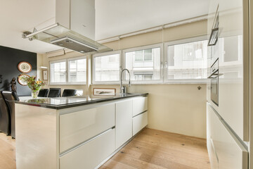 A bright, modern kitchen featuring sleek white cabinetry, hardwood flooring, and large windows that create a spacious ambiance.
