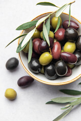 Fresh olives with olive branch in white bowl on marble table