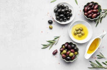 Bowls of various olives with olive oil and olive branches on marble table