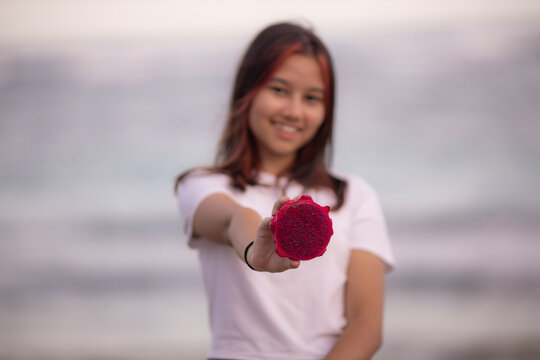 Portrait of girl holding half a dragon fruit in front of her. Selected focus on red dragon fruit. Blurred female.