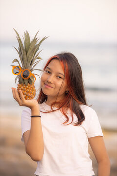 Close up portrait of teenager girl holding pineapple with sunglasses  in front of her face. Smiling face. Fruit concept.