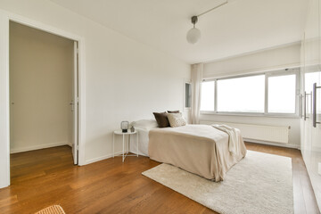 A beautifully designed minimalist bedroom featuring neutral tones, wooden flooring, and large windows that invite natural light, creating a serene atmosphere.