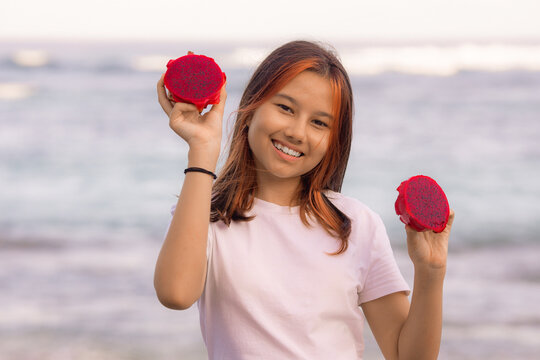 Portrait of attractive Asian teenager girl holding red dragon fruit halves. Outdoor photoshoot with dragon fruits. Bali.