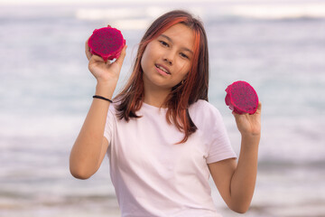 Portrait of beautiful Asian teenager girl holding red dragon fruit halves. Outdoor photoshoot with dragon fruits. Bali.