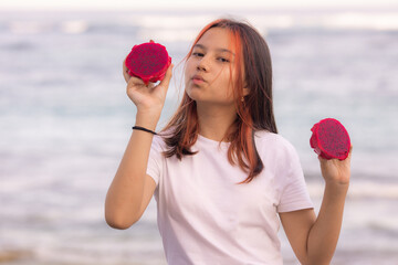 Portrait of charming Asian teenager girl holding red dragon fruit halves. Photoshoot with dragon fruits. Kissing lips.