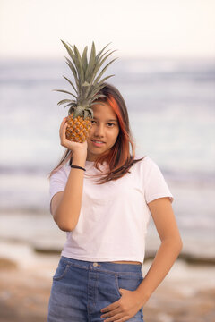 Teenager girl holding pineapple in front of her face. One eye closed by pineapple. Tropical fruit concept. Lifestyle.