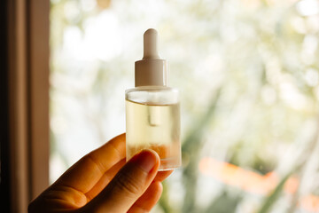Hand holding a glass bottle of natural skin serum. Care oil for moisturizing hair and scalp.
