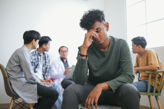 Portrait Of Stressed Young Indian Guy Against Blurry Group Therapy Session Background - Powered by Adobe