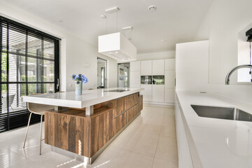 A sleek, modern kitchen showcasing minimalist design, featuring a central island with wood accents and large windows that enhance natural light.