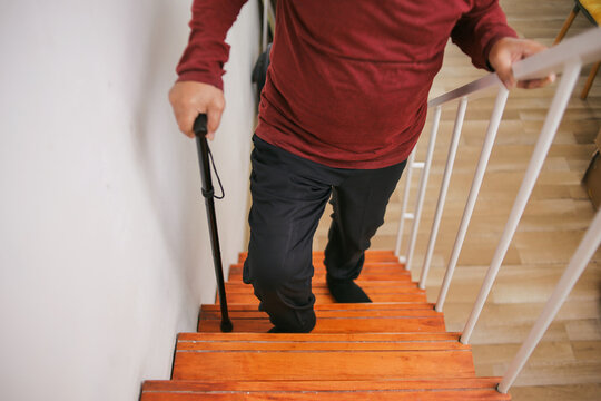 Senior Man Climbing Upstairs With Walking Stick At Home