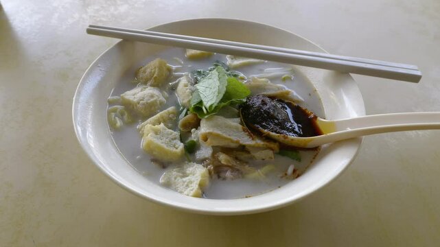 Close up of a bowl of curry mee or noodle in thick spicy gravy soup which is popular in Malaysia and Singapore. Toppings include cuttlefish, cockles, tofu and cogulated pig blood.