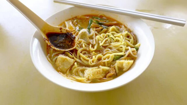 Close up of a bowl of curry mee or noodle in thick spicy gravy soup which is popular in Malaysia and Singapore. Toppings include cuttlefish, cockles, tofu and cogulated pig blood.