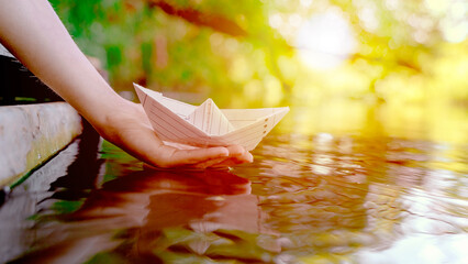 A child launches a paper boat into the water from the bridge