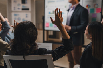 Businesswoman raising her hand to ask a question during a conference meeting, demonstrating active...