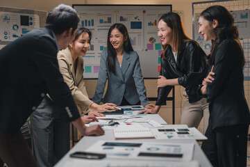 Group of five happy asian businesspeople working together on a project in a modern office at night, analyzing financial charts and discussing new strategies