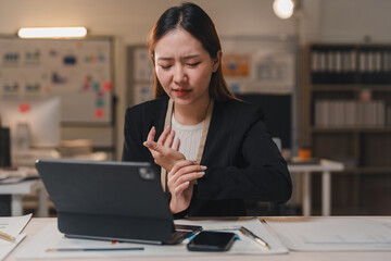 Young professional experiencing discomfort in her wrist while using a digital tablet, highlighting the physical strain of office work and the potential for repetitive strain injuries
