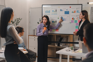 Businesswomen are leading a meeting in the office, presenting charts and statistics on a whiteboard, discussing company performance and strategies with colleagues