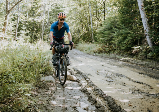 Male cyclist rides gravel bike along muddy dirt road in Maine