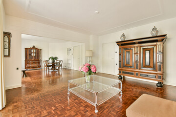 A spacious living room featuring stylish wooden furniture, decorative vases, and a vibrant floral arrangement, showcasing a blend of comfort and elegance.