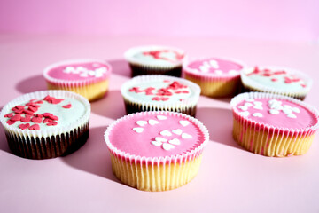 Sponge cupcakes with pink frosting and heart shaped sprinkles on a pink background