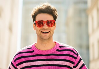 Smiling man wearing red sunglasses and a pink striped sweater