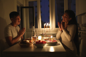 Couple clapping and praying before romantic candlelit dinner at home
