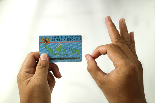 A person's hand holding Indonesian resident identification card or KTP and giving the right finger sign OK, isolated on white background.