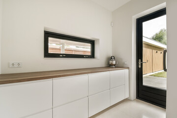 Bright and airy kitchen space featuring sleek cabinetry, wooden countertops, and a large window that invites natural light, enhancing the minimalist aesthetic.