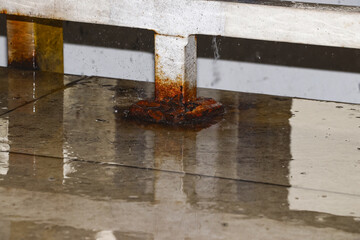 A rusty iron fence post was stuck to the floor which was wet from the rain, and there were a few splashes of water around the post