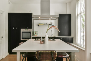 A stylish and contemporary kitchen featuring a sleek design with black cabinetry, a spacious table, and a bright atmosphere enhanced by natural light.