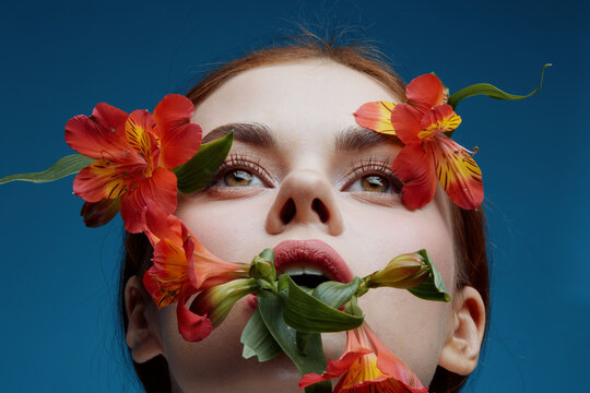 A close up portrait of a young woman with vibrant flowers accentuating her face, showcasing beauty and nature, ideal for concepts of femininity, self expression, and floral aesthetics