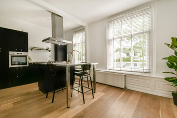 A sleek modern kitchen featuring an island, black cabinetry, and large windows that let in abundant natural light. The design emphasizes simplicity and functionality.