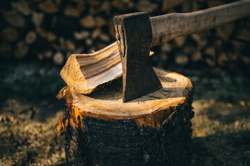 old ax stuck in a log on the background of firewood