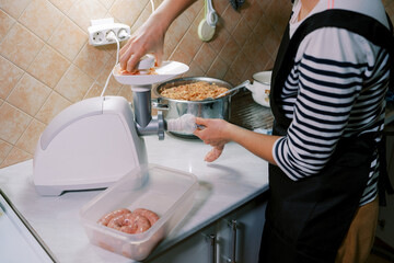 Chef stuffs the gut with minced meat on an electric meat grinder, pushing it with a pusher in the...