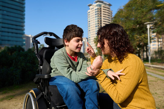 Happy child with disability communicating with special needs educator outdoors - cerebral palsy concept