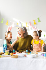 Happy family painting easter eggs wearing bunny ears at home in living room
