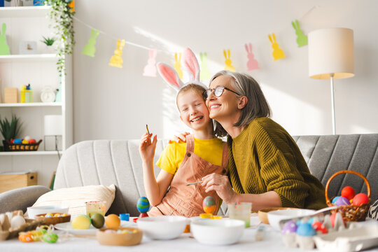 Naklejki Grandmother and grandchild painting easter eggs together at home
