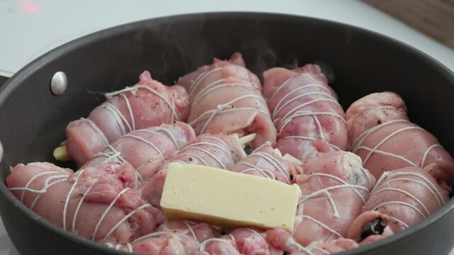 cook put piece of butter on resh raw chicken thighs meat filled rolls frying on pan, process of making healthy meal, food closeup