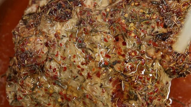 A close-up video of a large roasted pork piece in a white porcelain dish, basted with its own juices for extra tenderness and flavor.