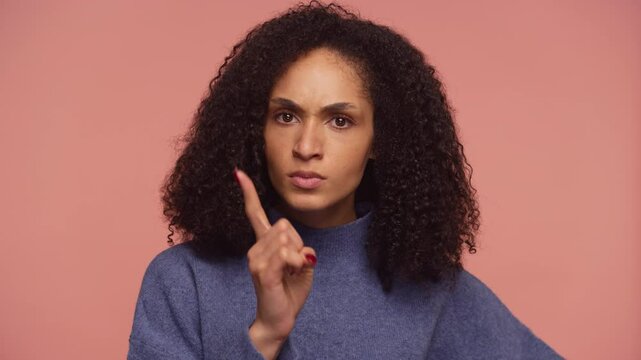 Serious woman making warning gesture on pink background