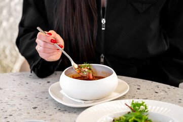A close-up of a hand holding a spoon, enjoying a flavorful stew from a stylish white bowl, accompanied by a fresh salad on a modern table setting.