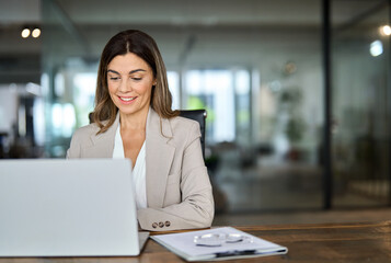 Happy mature business woman ceo entrepreneur in office using laptop at work, smiling professional...